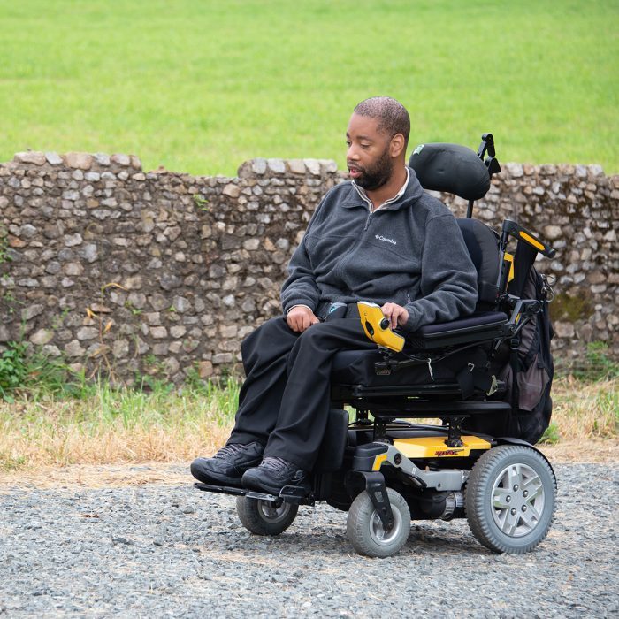 Artist Anthony LaFond in a wheelchair on a path by a rock wall.