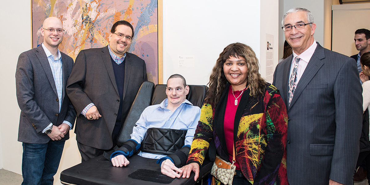 One man in a wheelchair and four able-bodied people standing in an art gallery