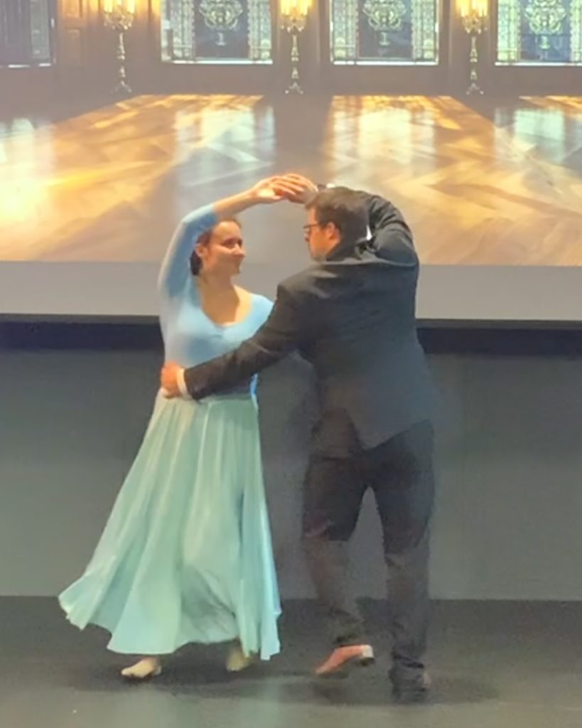 Young man in a grey suit jacket dancing with a woman in a floor length blue dress