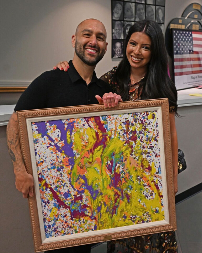 A man and a woman holding a framed abstract acrylic painting, with big smiles on their faces