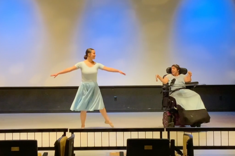 An able-bodied woman and a woman in a wheelchair dancing together on a stage.