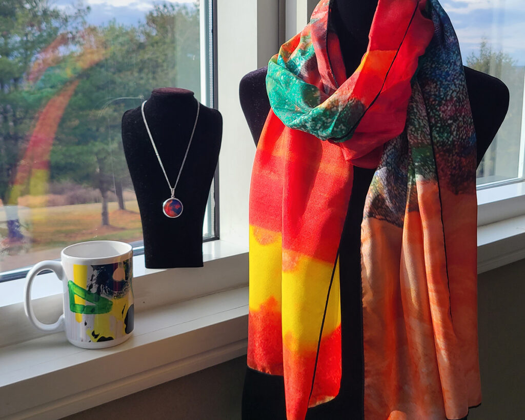 A ceramic mug, silver plated pendant necklace, and silk scarf from the Arts Access merchandise collection.