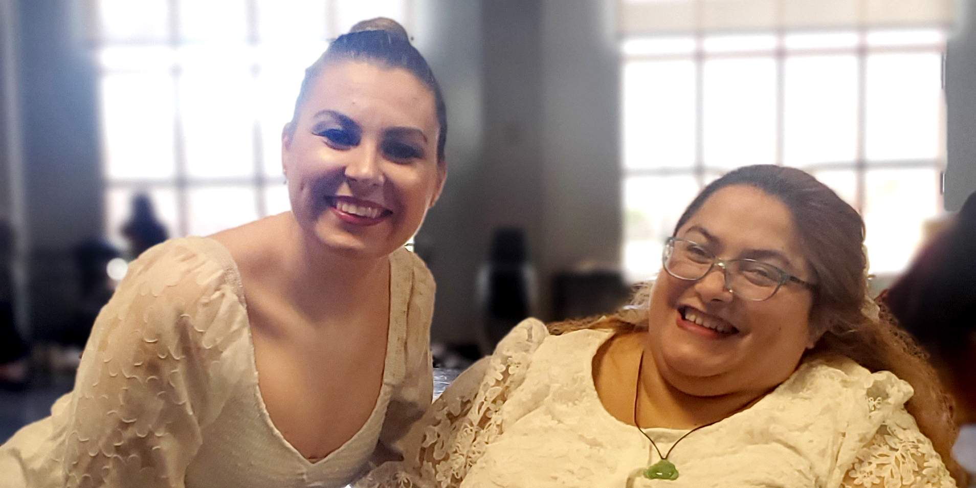 Two women, wearing white lace dresses, smiling.