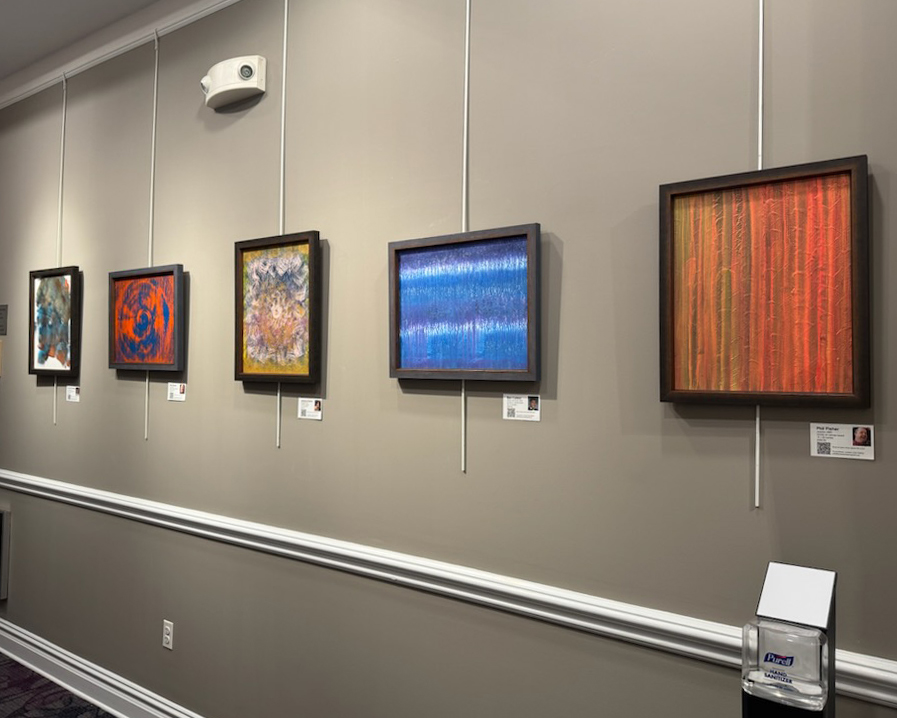 Five abstract acrylic paintings in black frames hanging on a beige gallery wall.