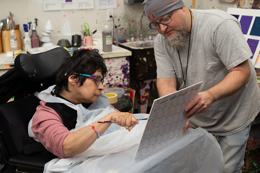 Nancy Soto, a woman who uses a wheelchair, painting with a facilitator in the Arts Access studio.